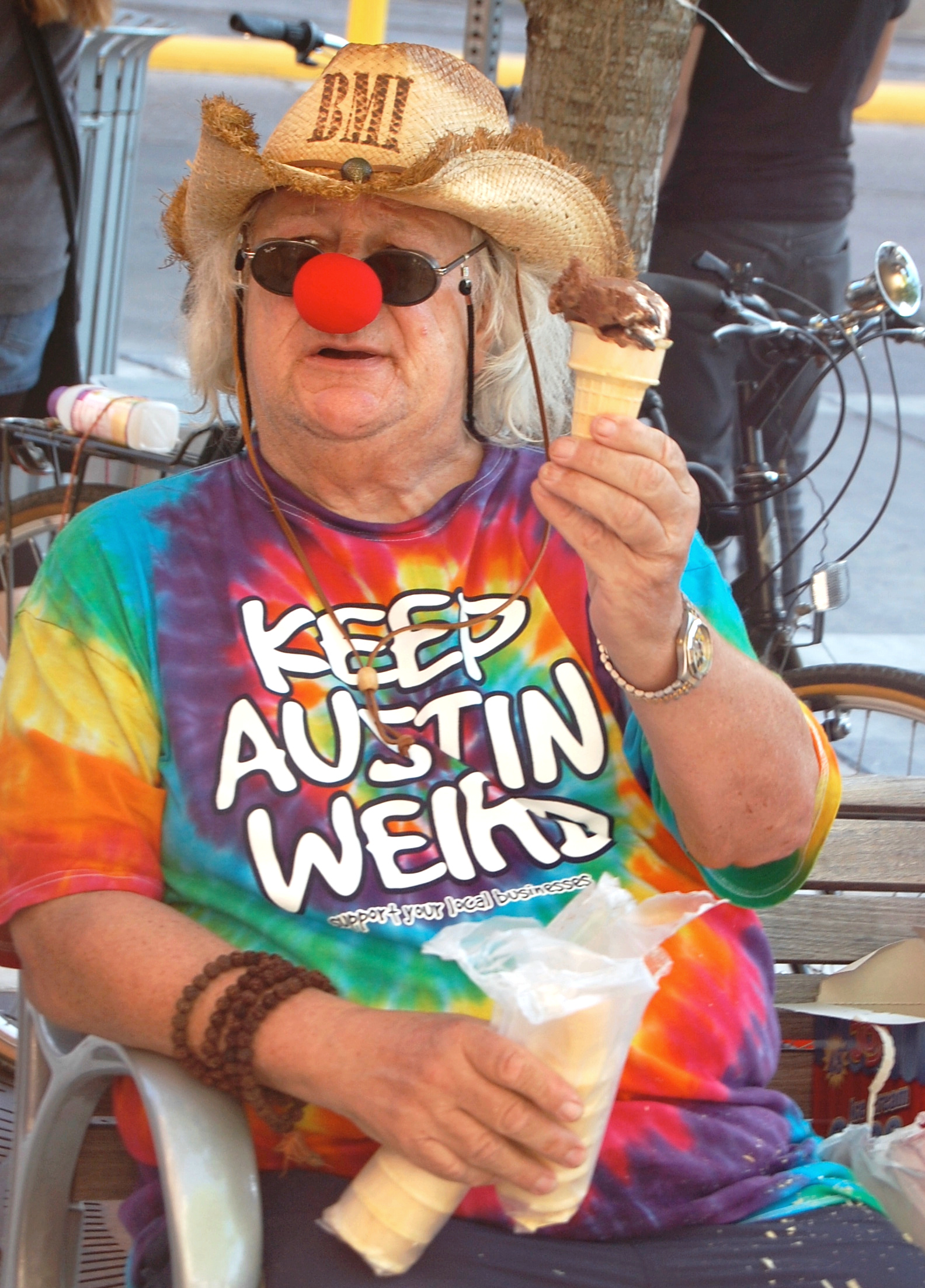 Wavy Gravy wearing a red clown nose, sunglasses, and a straw hat, holding an ice cream cone